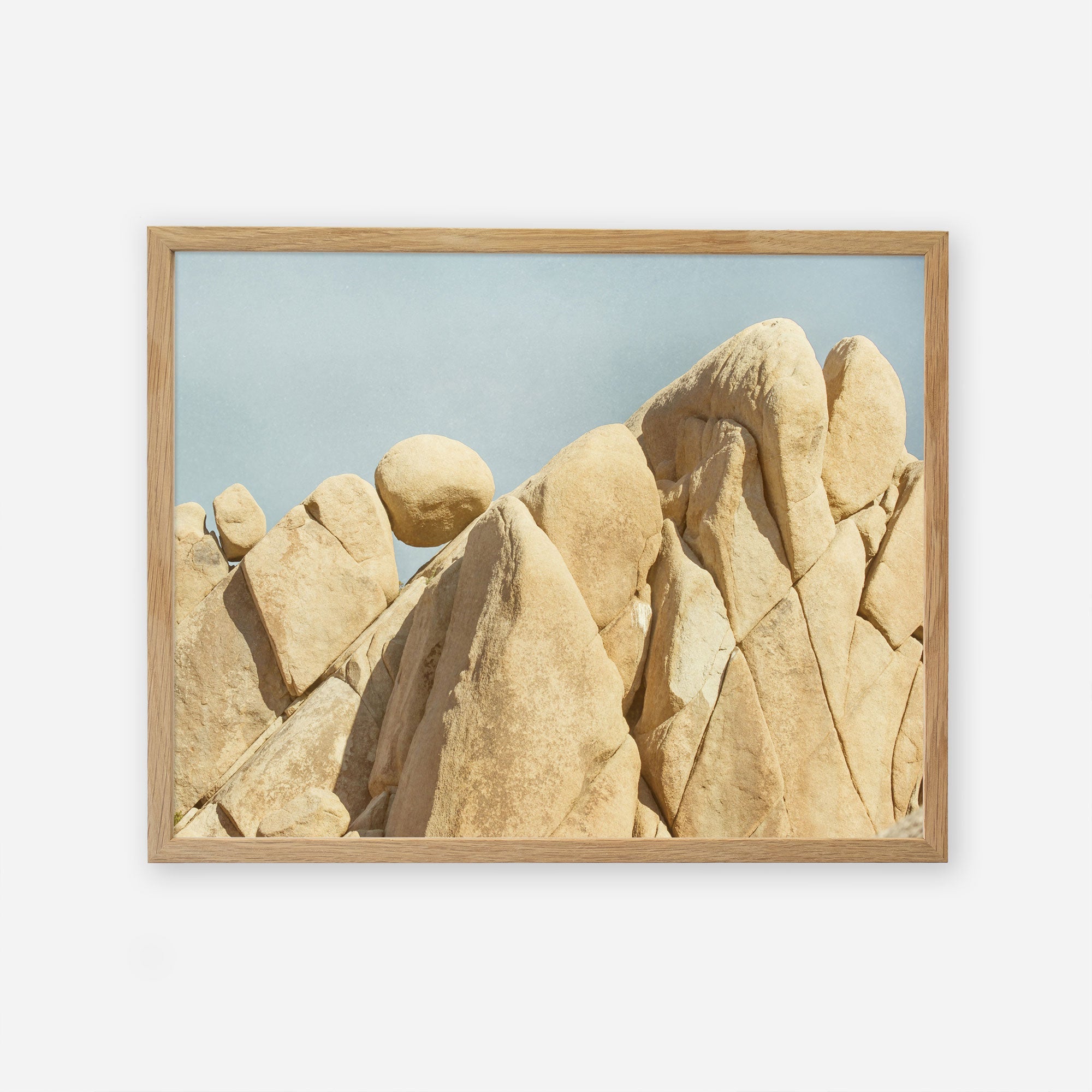 A framed photograph of a natural beige rock formation in Joshua Tree National Park, with jagged, smooth surfaces under a clear blue sky. The formation consists of clustered, vertical rock peaks. Offley Green&#39;s Joshua Tree Print, &#39;Rock Formations&#39; showcases this stunning scene beautifully.