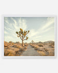 A serene desert landscape featuring a prominent Offley Green Joshua Tree Print, 'Path to Joshua' in the center, set against a pale sky with wispy clouds, and surrounded by sparse vegetation and rocky terrain near Palm Springs.