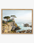 A framed painting depicting a scenic coastal landscape with rugged cliffs, a few windswept trees, and Offley Green's 'California Coastal Print, 'Lone Cypress' photography under a clear sky.