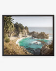A framed photograph of a Offley Green Big Sur Coastal Print, 'Julia Pffeifer' featuring rocky cliffs with a small sandy cove and turquoise waters, surrounded by lush greenery and tall palm trees.