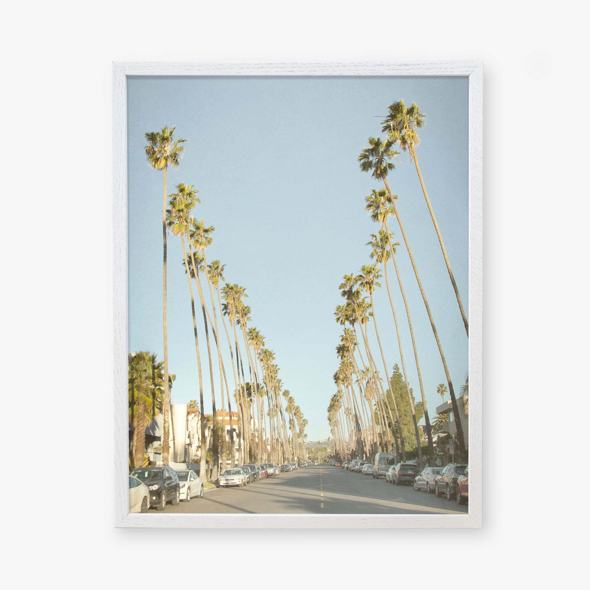 A framed photograph of Los Angeles Palm Tree Lined Street &#39;Sunset Boulevard Dreams&#39; by Offley Green, lined with tall palm trees on both sides, parked cars, and a clear blue sky.