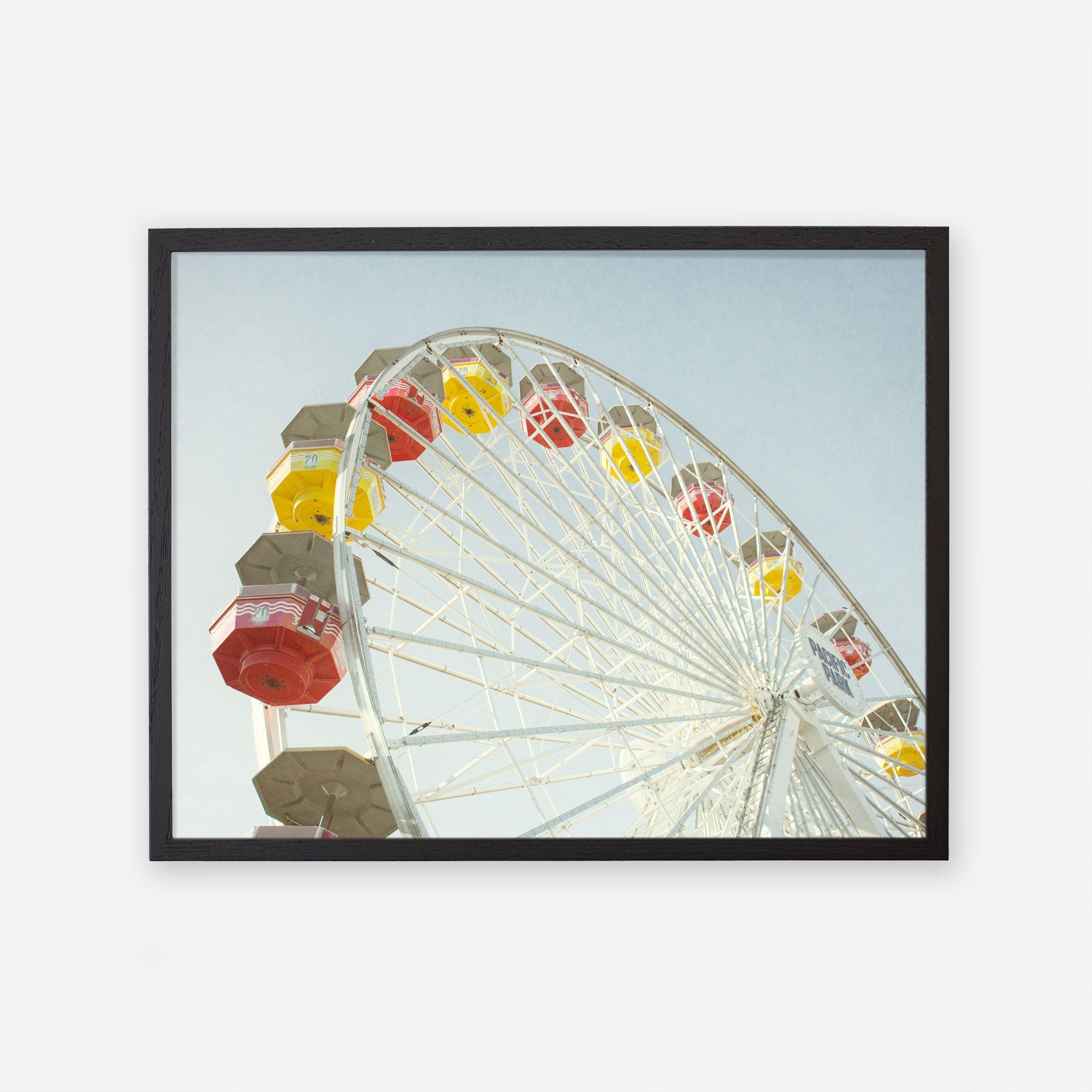 A framed photograph of the Offley Green Santa Monica Ferris Wheel Print, &#39;Ferris Above&#39; with colorful yellow and red cabins against a clear blue sky, angled view looking up from the base.