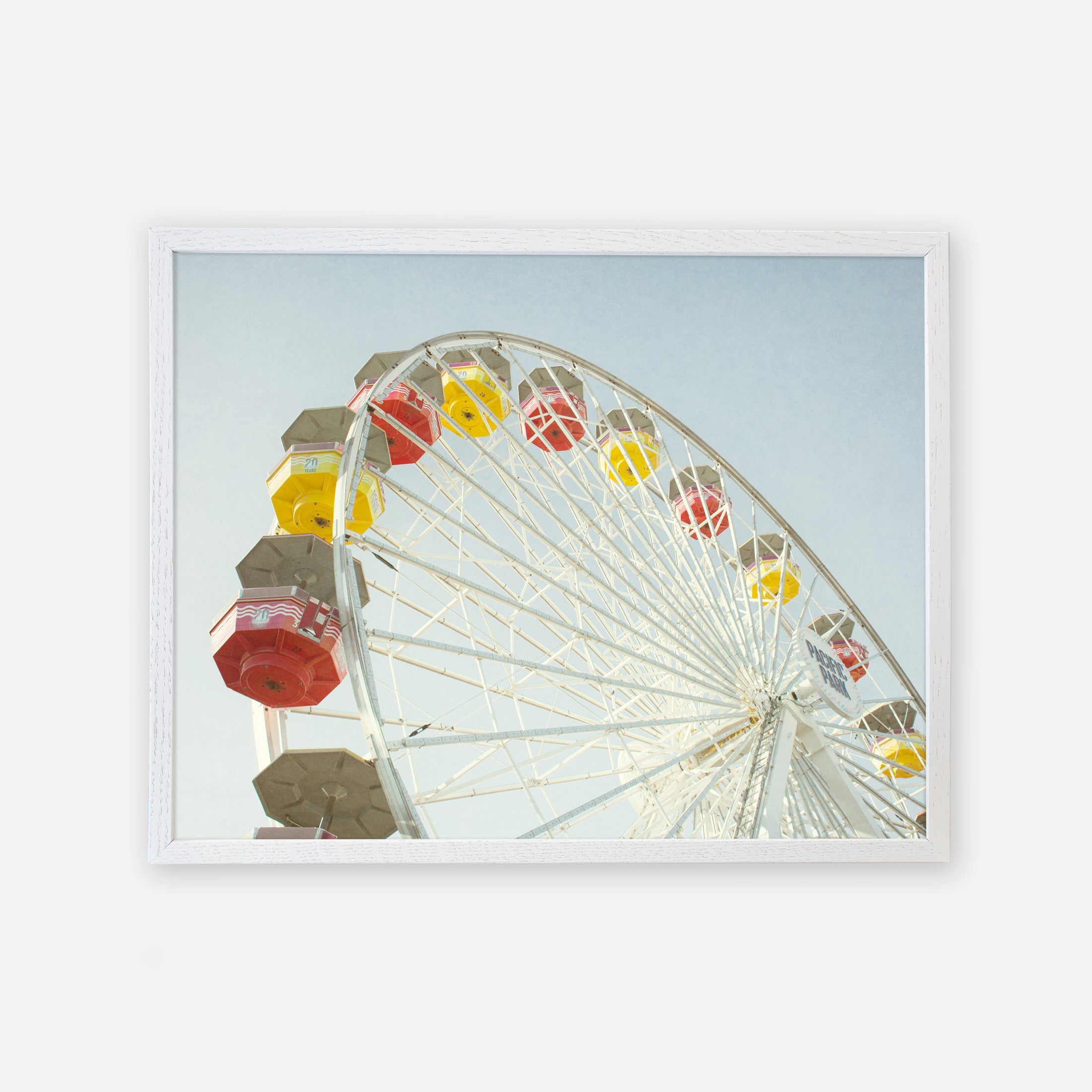 A colorful Santa Monica Ferris Wheel Print with red, yellow, and white cabins against a clear sky at Santa Monica Pier, framed as if it is a picture hanging on a wall.