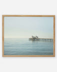 A framed photograph depicting a tranquil ocean view with Malibu Pier extending into the water, topped by a small building, set against a clear sky.