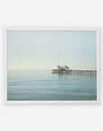 A framed photograph of a tranquil seascape with Malibu Pier extending into the calm sea under a soft, pale sky. The image conveys a serene, timeless atmosphere featuring the Coastal Print of Malibu Pier in California 'All Calm in Malibu' by Offley Green.