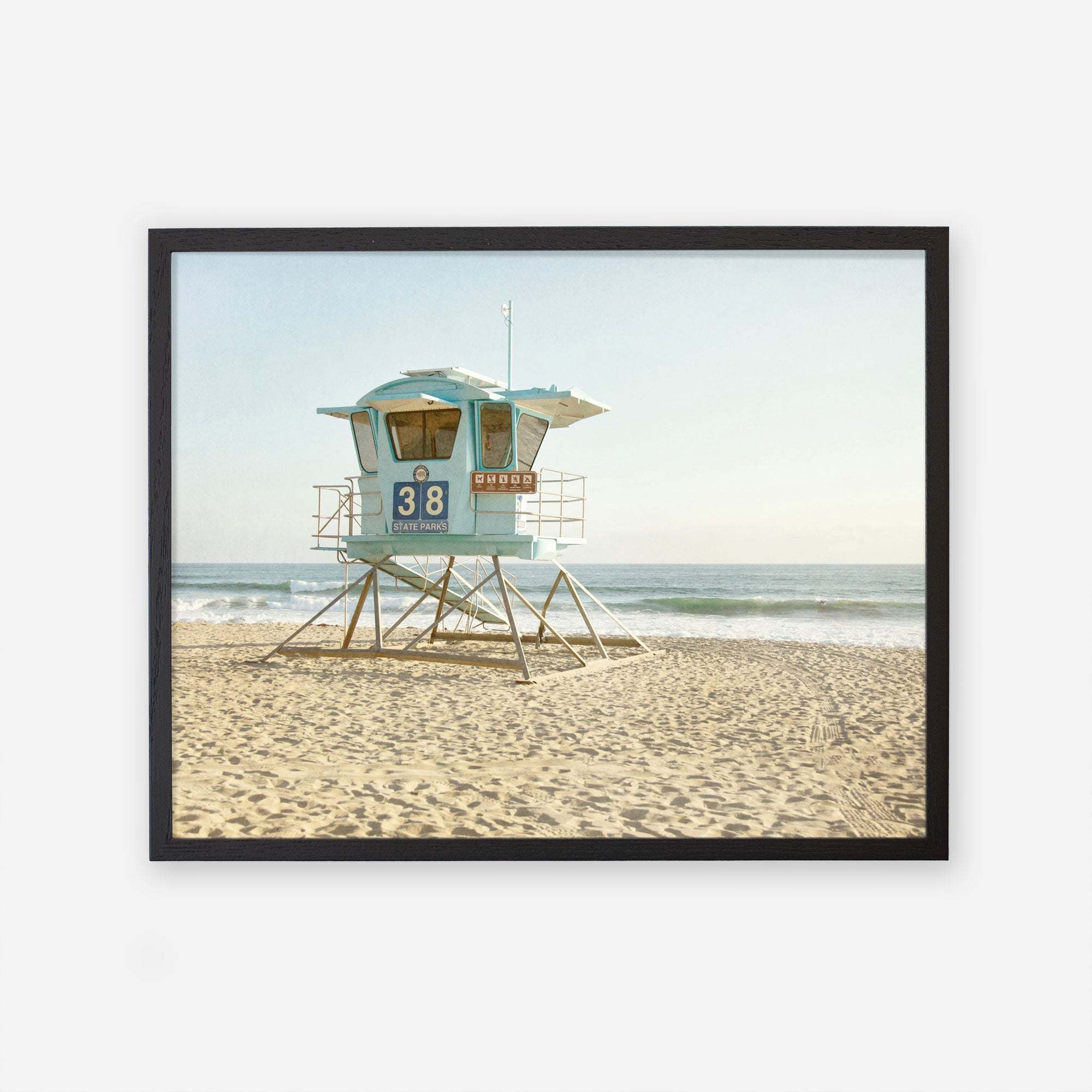 An unframed California Coastal Print of &#39;Carlsbad Lifeguard Tower&#39; on a sandy beach, with calm ocean waves in the background under a clear sky by Offley Green.