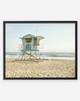 An unframed California Coastal Print of 'Carlsbad Lifeguard Tower' on a sandy beach, with calm ocean waves in the background under a clear sky by Offley Green.