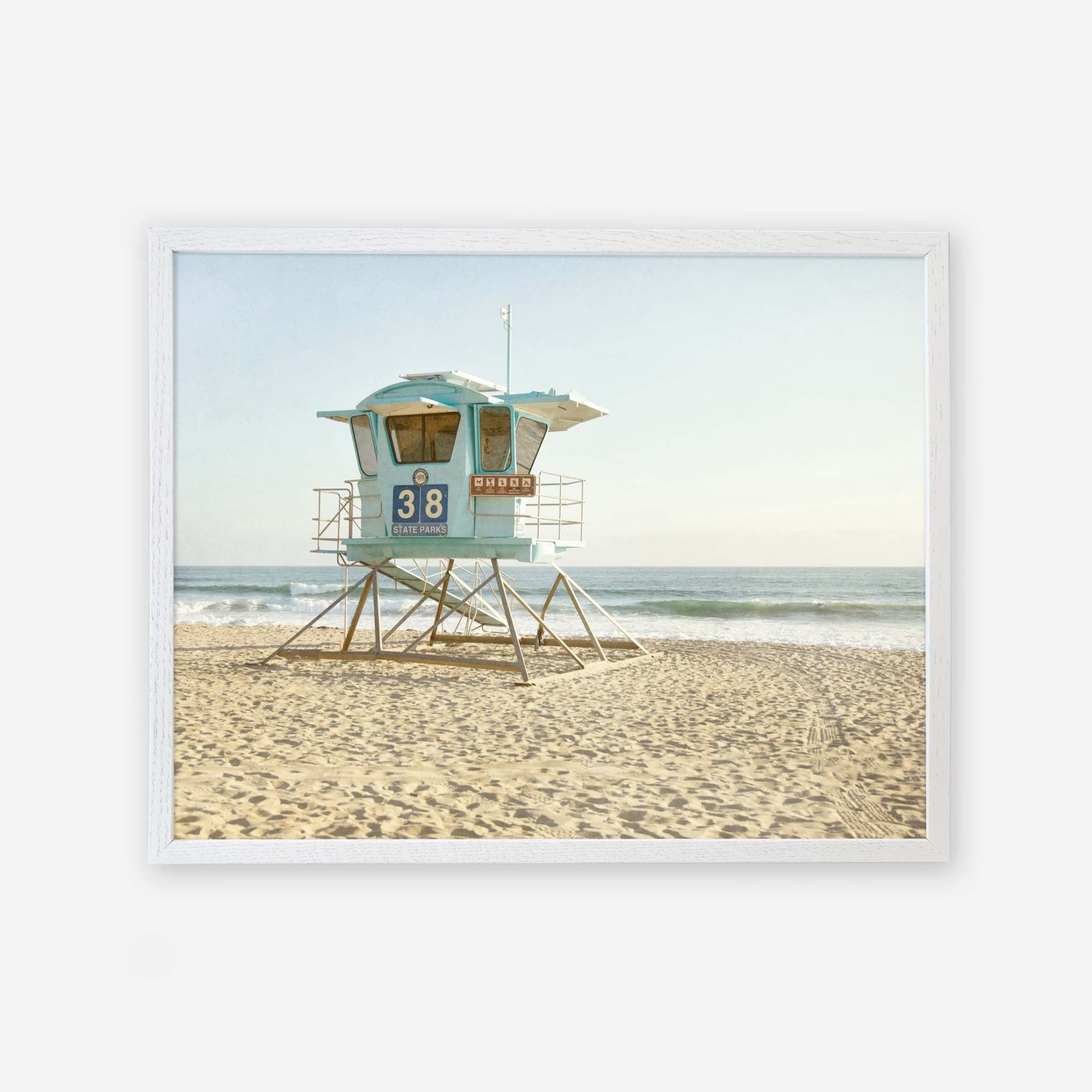 A picturesque Offley Green California Coastal Print, &#39;Carlsbad Lifeguard Tower&#39; scene featuring lifeguard tower 38 on sandy soil with the ocean in the background, set against a clear sky.