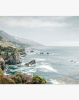 A scenic view of a misty coastline along California Highway 1 with rugged cliffs and waves crashing against the shore, under a soft cloudy sky. The landscape includes lush greenery and distant rocky outc featuring the Offley Green Big Sur Landscape Print, 'Rocky Rocks'.