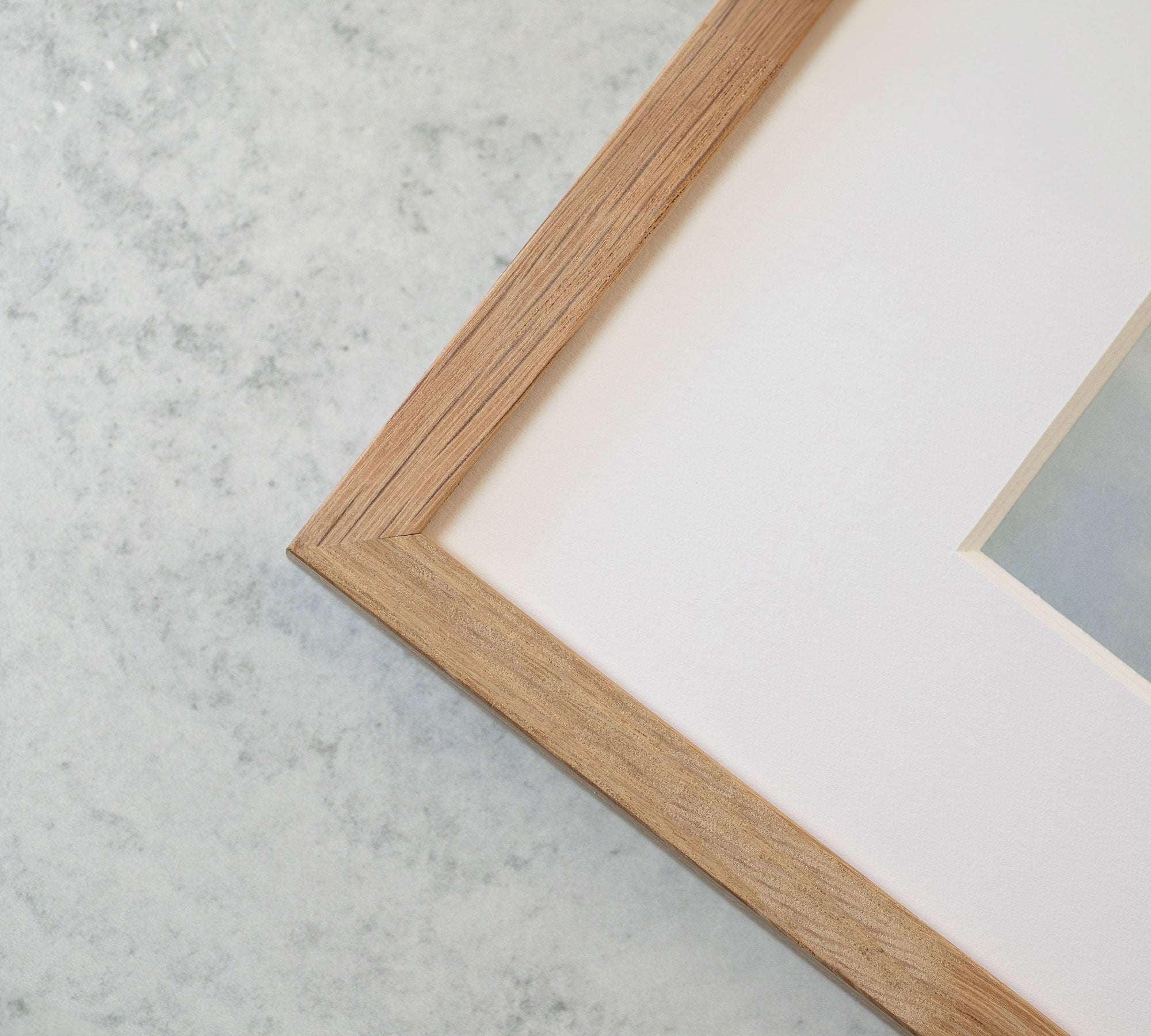 Close-up of a corner of a wooden picture frame on a marble background, showcasing part of the frame and white matting inside, designed to hold Offley Green&#39;s Big Sur Landscape Print, &#39;Rocky Rocks&#39;.