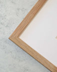 Close-up of a corner of a wooden picture frame on a marble background, showcasing part of the frame and white matting inside, designed to hold Offley Green's Big Sur Landscape Print, 'Rocky Rocks'.
