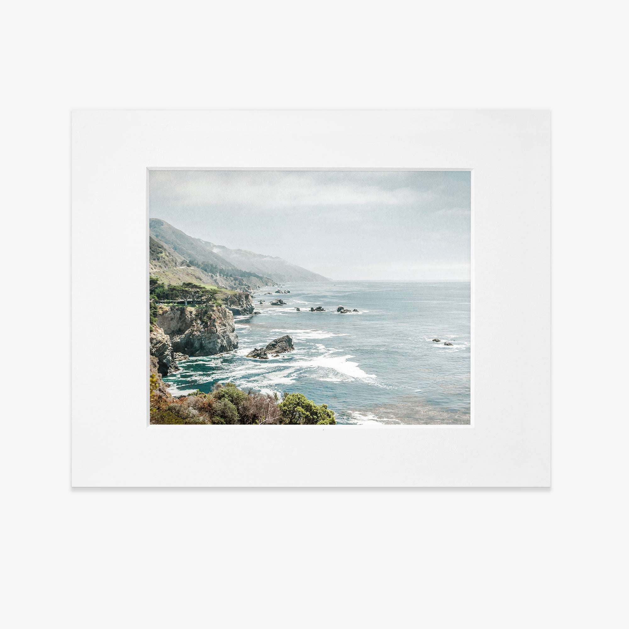 A matted print depicting a scenic coastal landscape along Big Sur with rocky cliffs and the ocean, viewed from a high vantage point under a hazy sky -  Offley Green&#39;s Big Sur Landscape Print, &#39;Rocky Rocks&#39;.