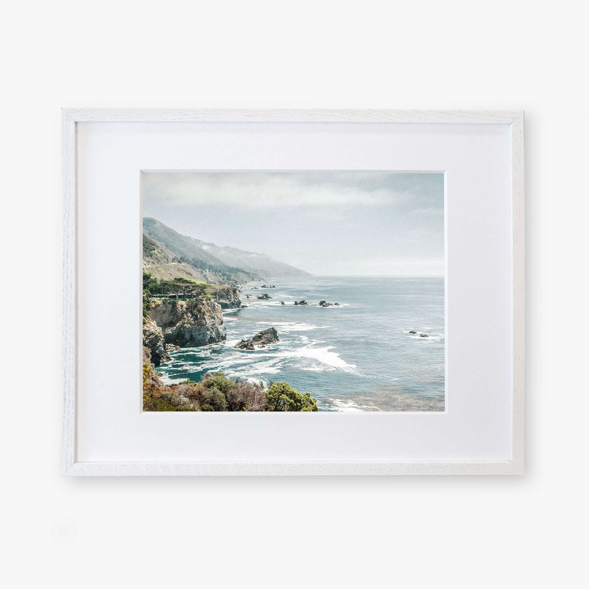 A framed photograph of a scenic Big Sur view, showing a rocky cliffside descending into a foggy ocean with sparse vegetation and an overcast sky - Offley Green&#39;s Big Sur Landscape Print, &#39;Rocky Rocks&#39;