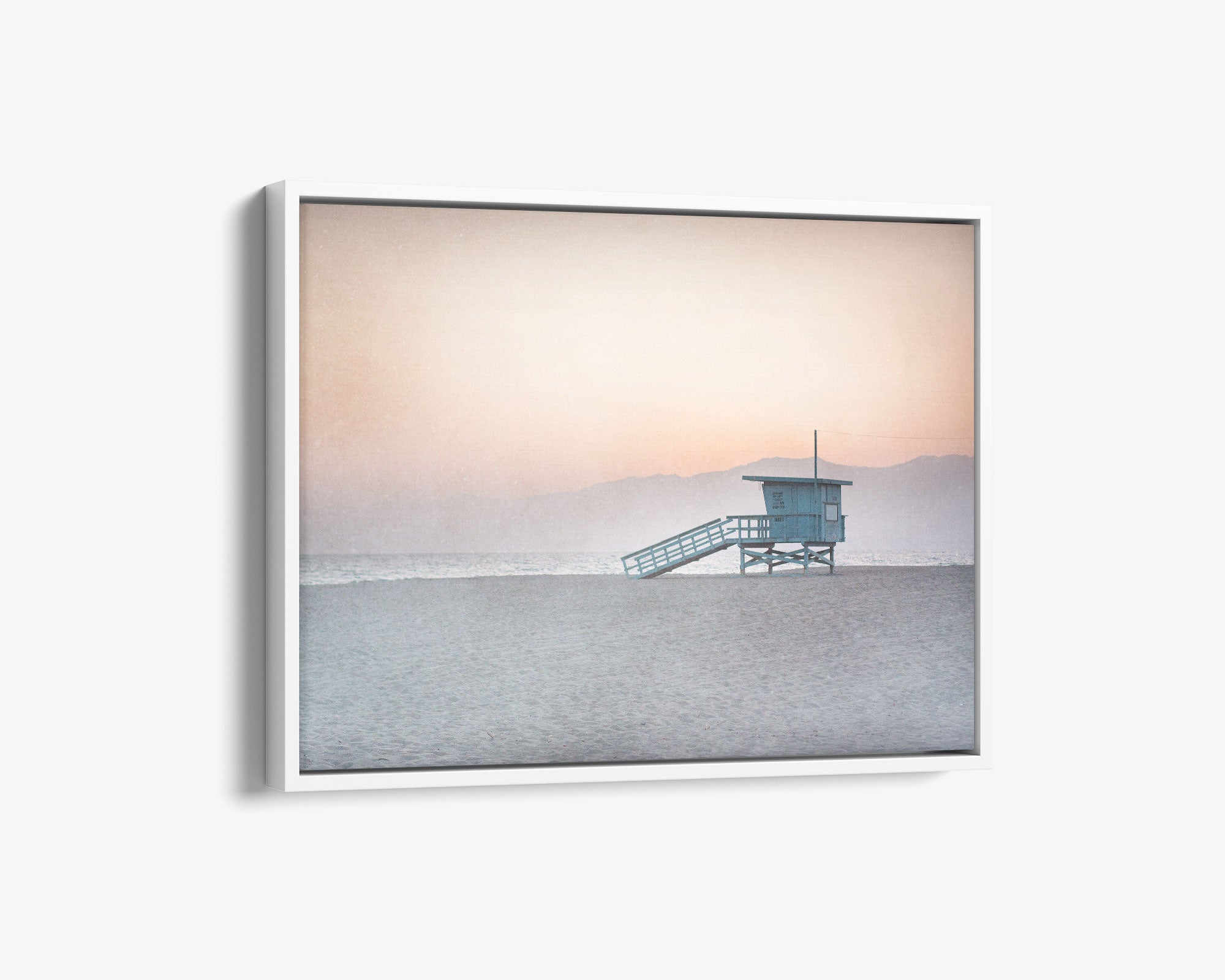 A framed Pink Coastal Wall Art photograph of a &#39;Lifeguard Tower&#39; on Venice Santa Monica Beach by Offley Green, with gentle hues of pink and blue in the sky and a soft glow reflecting off the ocean.