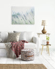 A cozy living room corner with a white sofa adorned with colorful cushions, a knit blanket, a small wood side table with a lamp, and a large Offley Green canvas gallery wrap of Rustic Farmhouse Canvas Wall Art, 'Buds of Lavender' on the wall.