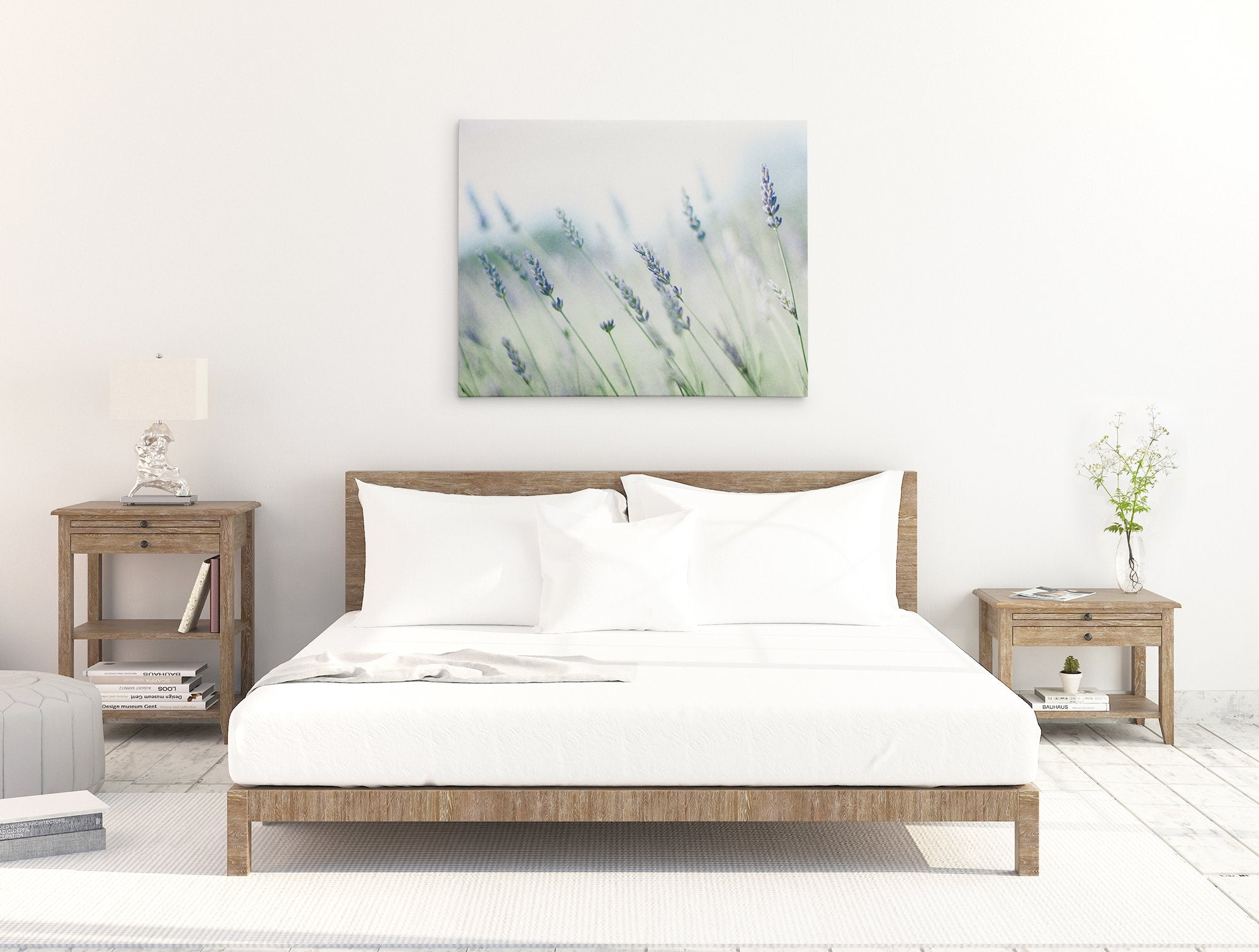 A minimalist bedroom with a large bed covered in white bedding, flanked by wooden nightstands and a serene Offley Green Rustic Farmhouse Canvas Wall Art, &#39;Buds of Lavender&#39; above the bed.